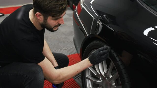 A mechanic wearing black t-shirt and black gloves blackening black car's tyre. . High quality 4k footage