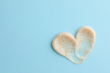 Fototapeta premium Samples of face scrub in shape of heart on light blue background, top view. Space for text