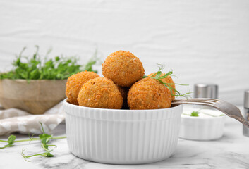 Bowl of delicious fried tofu balls with pea sprouts on white marble table