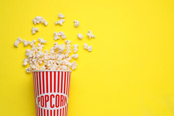 Overturned paper cup with delicious popcorn on yellow background, flat lay. Space for text