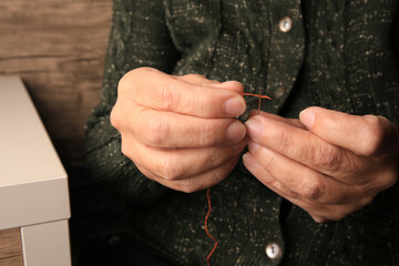 Fototapeta premium Closeup view of woman threading needle indoors. Sewing equipment