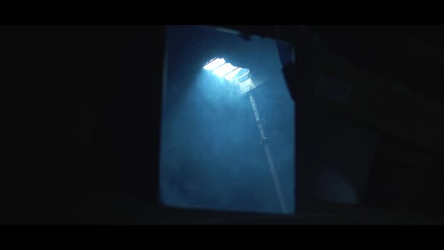 Old garage with blue light. Atmosphere dark place full of smoke. Strang and mystery man in black coat and black hat is walking 