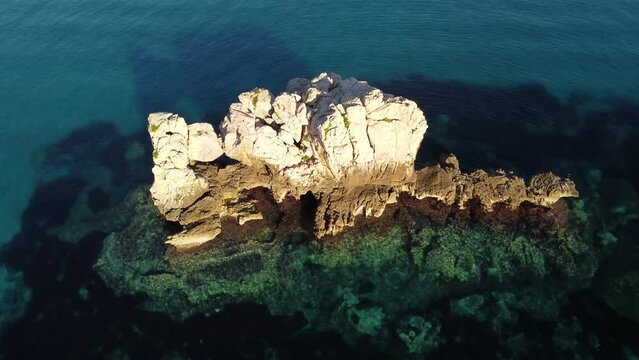 Aerial flying above crystal clear turquoise Sardinian sea water, flying forward towards white rock formation, sunset