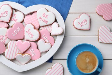 Delicious heart shaped cookies and cup of coffee on white wooden table, flat lay