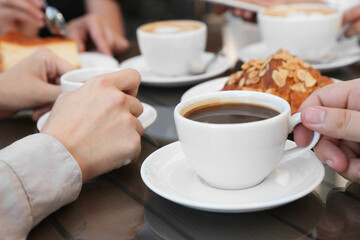 Friends drinking coffee at wooden table in outdoor cafe, closeup