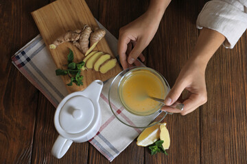Woman making aromatic ginger tea at wooden table, top view