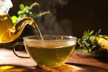 Pouring aromatic herbal tea into cup on wooden table, closeup