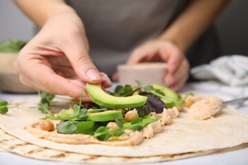 Woman making delicious hummus wrap with vegetables at table, closeup