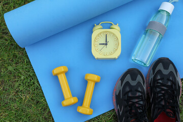 Alarm clock and morning exercise set on green grass, flat lay