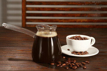 Glass turkish coffee pot with hot drink and beans on wooden table