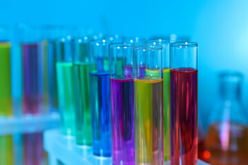 Many test tubes with colorful liquids on light blue background, closeup
