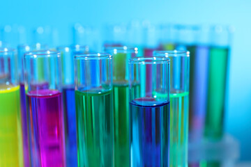 Many test tubes with colorful liquids on light blue background, closeup