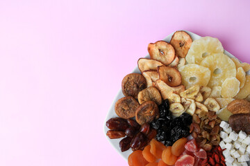 Plate with different dried fruits on violet background, top view. Space for text
