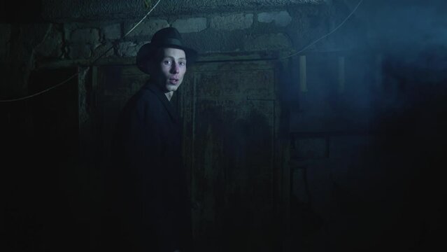 Old garage with blue light. Atmosphere dark place full of smoke. Strang and mystery man in black coat and black hat is talking