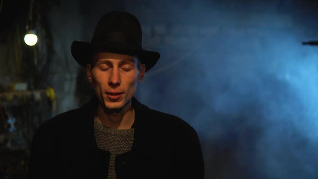 Old garage with blue light. Atmosphere dark place full of smoke. Strang and mystery man in black coat and black hat is talking