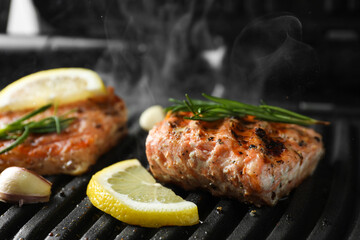 Tasty salmon cooking with rosemary and lemon slice on electric grill, closeup