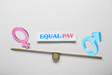Equal pay concept. Gender symbols on miniature seesaw against light grey background
