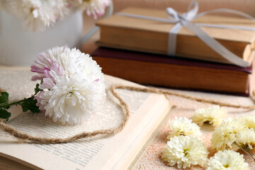 Obraz na płótnie Canvas Book with chrysanthemum flowers as bookmark on beige textured table, closeup. Space for text