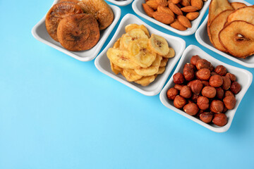 Bowls with dried fruits and nuts on light blue background, above view. Space for text
