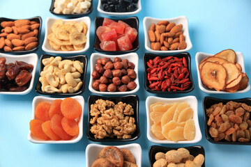 Bowls with dried fruits and nuts on light blue background