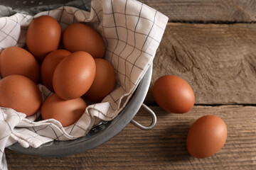 Chicken eggs in colander and napkin on wooden table