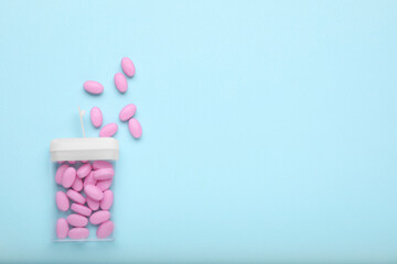 Tasty pink dragee candies and container on light blue background, flat lay. Space for text