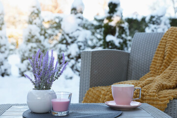 Candle, potted flowers and cup of hot drink on coffee table outdoors. Cosy winter