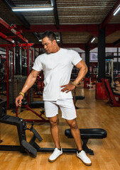 A gym athlete wearing a white blank shirt doing a pose at a gym