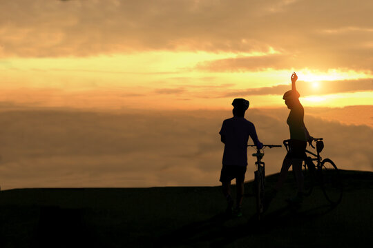 A silhouette of a cyclist standing looking at the clouds on the mountain peak in the sunrise.