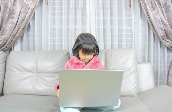 Asian girl wear headphone using laptop, studying online at home.