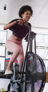 Vertical video of determined african american woman working out at a gym on exercise bike