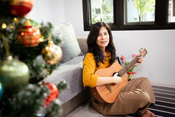Young asain female musician sit in armchair alone compose instrumental song using classic guitar at...