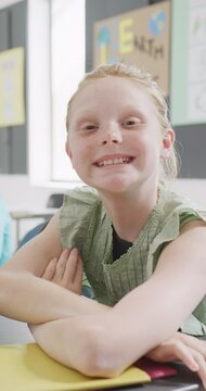 Vertical video portrait of happy caucasian schoolgirl sitting at desk in class, copy space