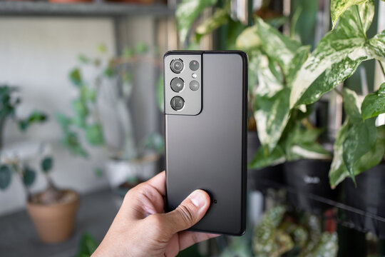 PENANG, MALAYSIA - MAR 11, 2021: Hand holing the latest Samsung Galaxy S21 Ultra 5G Phantom Black color and showing the back of the phone and brand new camera lens in green leaf background