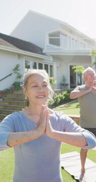 Vertical video of happy diverse senior couple practicing yoga in garden