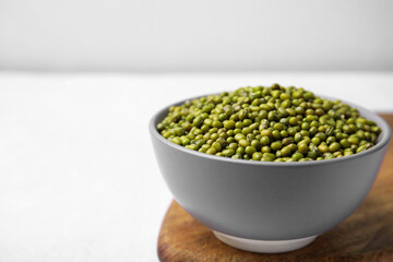 Bowl with green mung beans and wooden board on white table, closeup. Space for text
