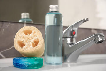Fototapeta na wymiar Loofah sponge and cosmetic products on sink in bathroom, closeup