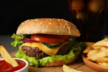 Delicious burger, ketchup and french fries served on wooden tray, closeup