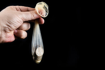 A condom filled with 25 American cents in a man's hand  against the black background 