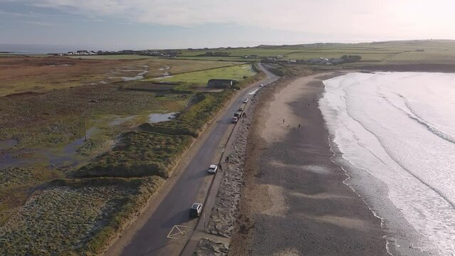 Coastal road, winter sun and few walker on a sandy beach with foaming waves in slow motion.