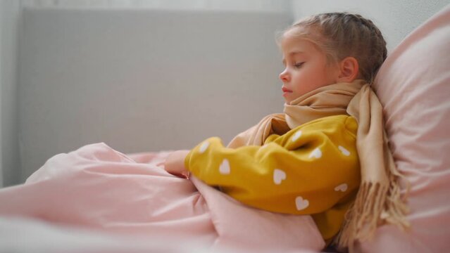 Child girl in plaid and scarf suffering from Coronavirus or allergy, sneezes snot into napkin on sofa at home Side view slow motion