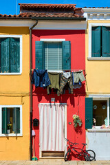 Picturesque facade of house in Burano, Italy, with vibrant red and yellow colors, bike parked and hanging clothes under the window.