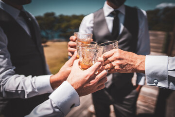close up of hands as men in shirts and waistcoats clinking whiskey glasses together in cheers