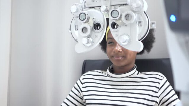 African teen girl Doing Eye Test On Phoropter, African teen girl checking on her eye with optometry machine.
