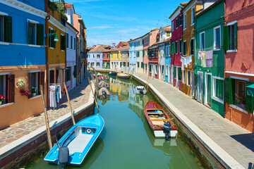 Fototapeta na wymiar Panoramic view of canal with boats in Burano, Italy, surrounded by picturesque colorful houses decorated with plants, flowers and hanging clothes.