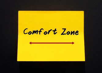 A yellow note pad with red written message text COMFORT ZONE , stick on the dark wall - concept of...