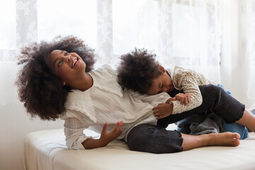 Two African American child girls playing together on bed at home. kids, play and holiday concept