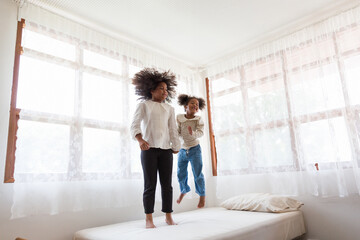 Two African American child girls playing together and jumping on bed at home. kids, play and holiday concept