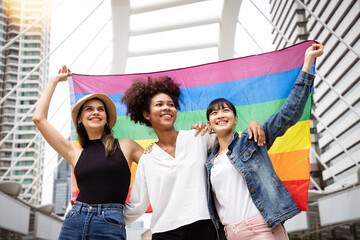 Diversity young gay women with Asian gay waving pride rainbow flag in their backs supporting LGBTQ...