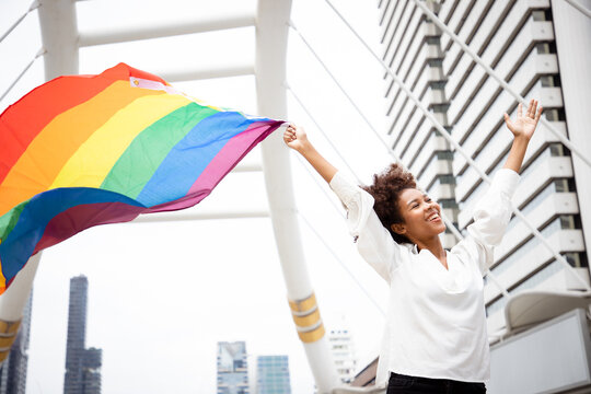 Portrait of young lesbian woman waving pride rainbow flag in their backs supporting LGBTQ pride in the cityscape. Independence and gender diversity. Supporters of the LGBT community. Safe zone.